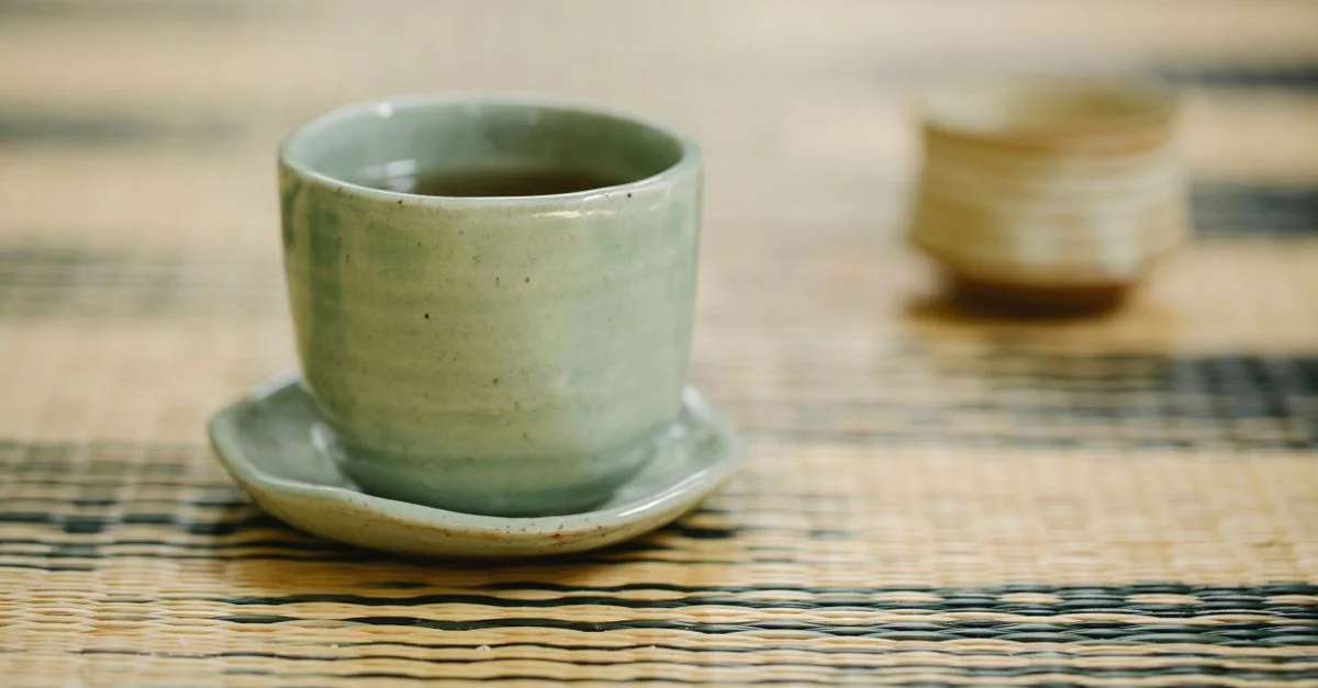 Stylée tasse en céramique verte avec soucoupe sur un tapis en osier tissé, créant une ambiance sereine pour le thé.