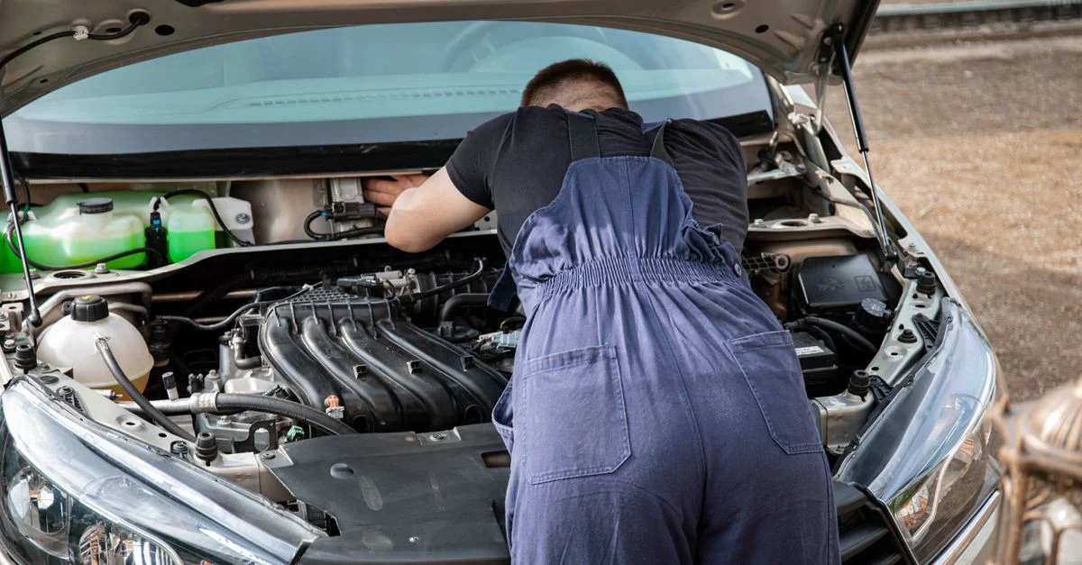 Un mécanicien automobile effectuant l'entretien du moteur d'une voiture à l'extérieur, montrant ses compétences mécaniques.